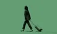 an Asian woman dragging a suitcase against a greenbackground
